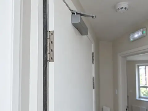 Fire door edge showing the intumescent seal, steel hinges and overhead closer